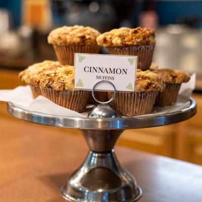 A display of cinnamon muffins on a silver stand with a labeled sign.
