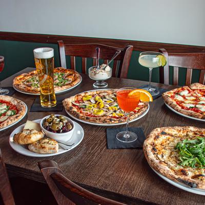 Various pizzas served on the table with a appetizer and drinks.