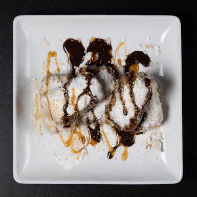 Beignets covered in powdered sugar, chocolate syrup, and caramel.