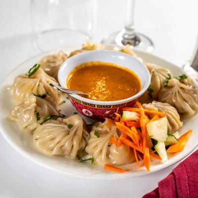 A plate of steamed momo dumplings served with a chutney in a decorative bowl.