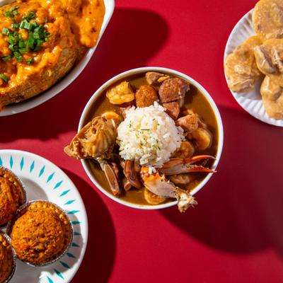 Gumbo bowl with rice, sausage, and seafood, surrounded by other dishes.