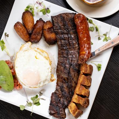 Skirt steak with a pork strip, a fried egg, sausage, and plantains.