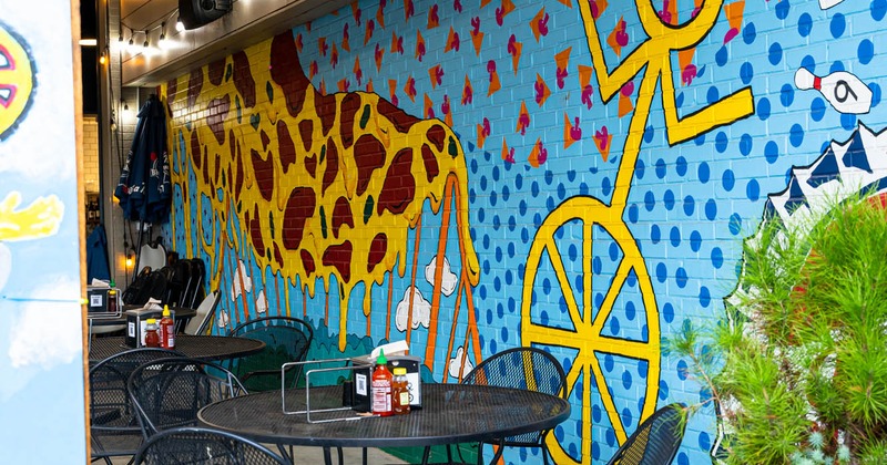Tables and seats by a wall decorated with a large mural art