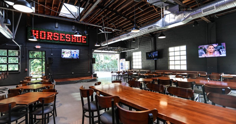Dining tables and seats, music stage by a wall with Horseshoe neon light sign