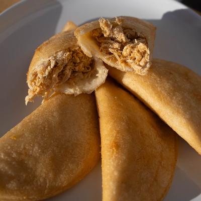 Four empanadas on a white plate, one cut open to show shredded meat filling.