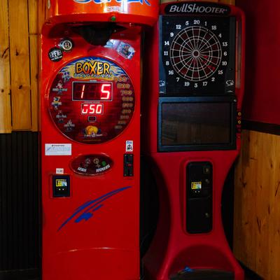Electronic dartboard featuring a vibrant red cabinet beside a boxing arcade machine.