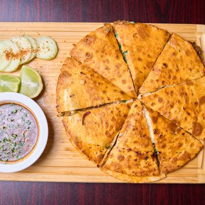Birria pizza served with consommé, lime wedges and sliced cucumber.