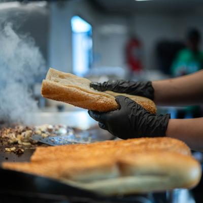 Cheesesteak sandwich being prepared on a griddle.