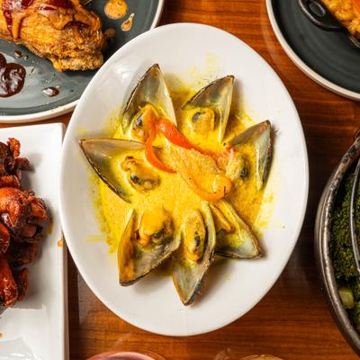 Mussels served in a creamy, yellow-toned broth with pepper slices.