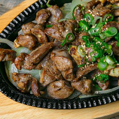A platter of grilled meat with onions, topped with green onions and sesame seeds.