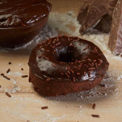 Baked chocolate donut with chocolate glaze and chocolate sprinkles on a floured board.