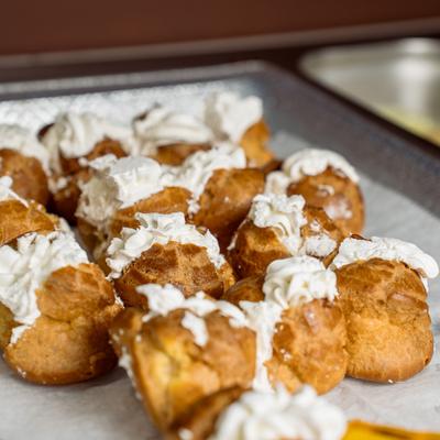 A tray of golden cream puffs generously topped with whipped white cream.