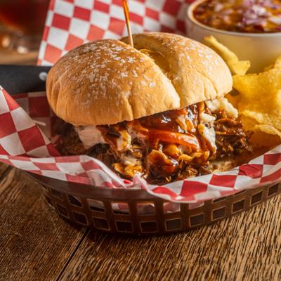Barbecue pulled pork sandwich served with potato chips and a bowl of chili.