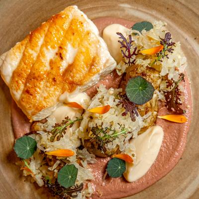 Pan-seared white fish fillet, served over a pink sauce with various garnishes.