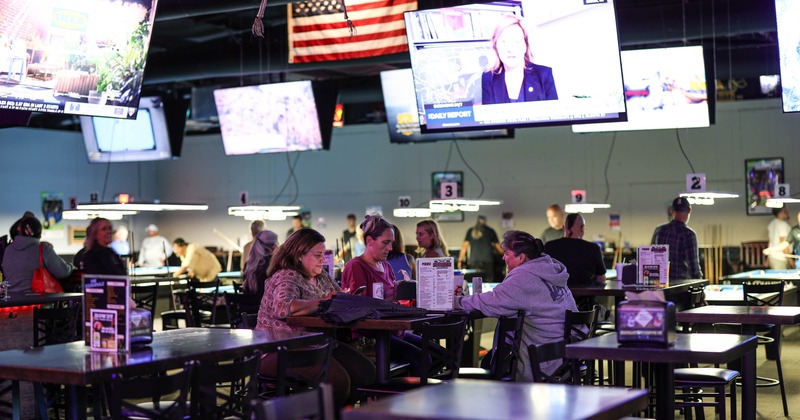 Interior, patrons seated at dark tables, multiple mounted TVs displaying sports and news
