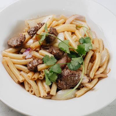 Macaroni with beef pieces and onions in white bowl.