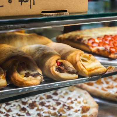 Assorted rolls and pizzas displayed in a glass case.