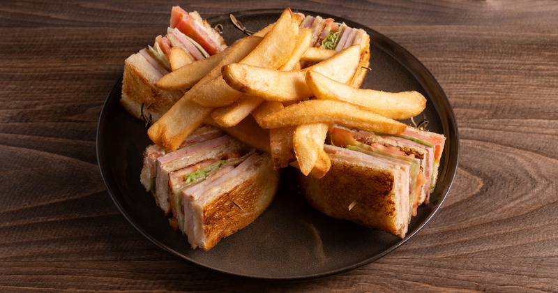 Club sandwich served with fries on a dark plate