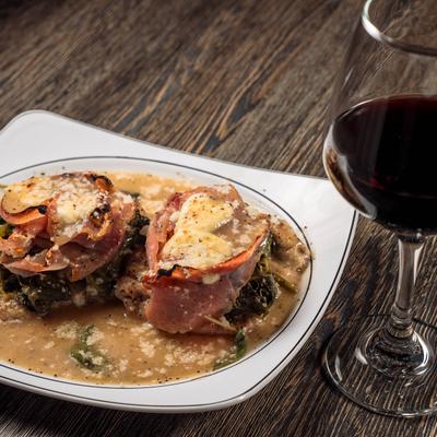 Veal topped with prosciutto, spinach, and fresh mozzarella, accompanied with wine.