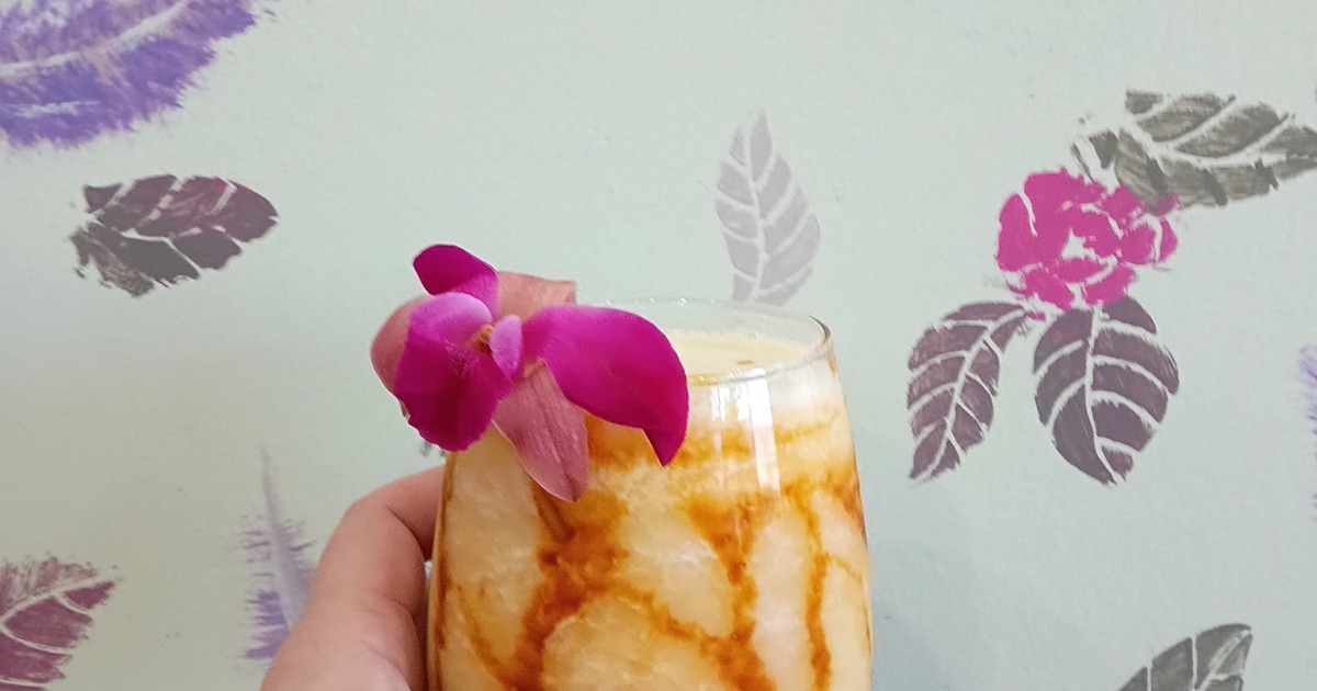 Hand holding a layered tropical drink garnished with a vibrant purple orchid