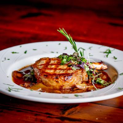 Grilled steak on a white plate, garnished with fresh herbs and microgreens.