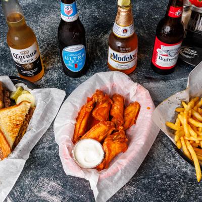 Bar food including wings, fries, and sandwiches sits next to four beer bottles.
