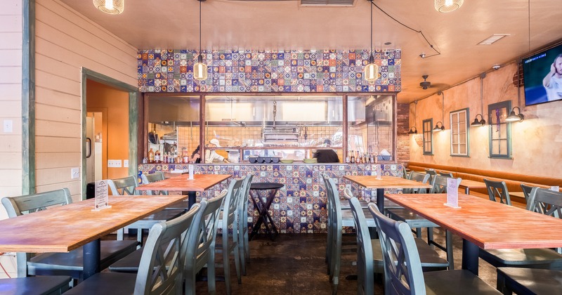 Interior of a cozy Mexican restaurant with an open kitchen area, wooden tables, and high chairs
