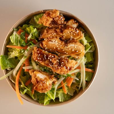 Asian-style crispy chicken salad topped with sauce and sesame seeds.