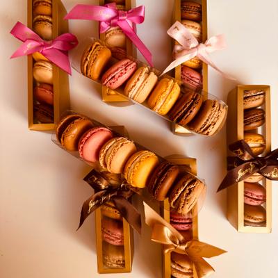 Assorted macarons presented in small boxes tied with ribbons.