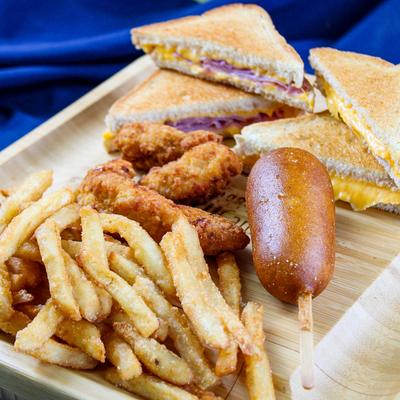 Kids menu, grilled cheese, chicken tenders, corn dog and fries on a wooden plate.