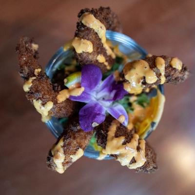 Fried shrimp served in a glass, topped with sauce and purple flower, top view.