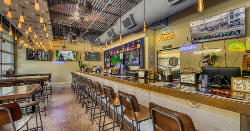 Modern taco restaurant interior with bar stools, pendant lighting and TVs.