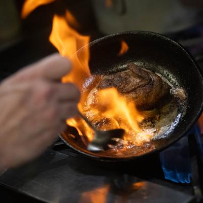 Hands preparing food in a flaming frying pan.