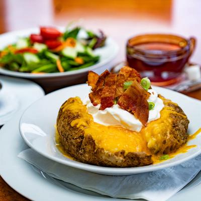 A loaded baked potato topped with cheese, bacon, and sour cream, served with a salad.