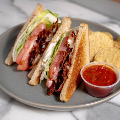 BLT sandwich served with chips and a dipping sauce.