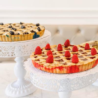 Raspberry lattice pie and blueberry lattice pie on elegant white cake stands.