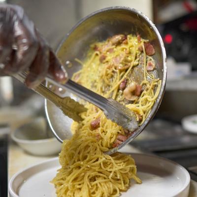 Creamy spaghetti carbonara dish being plated from a metal skillet.