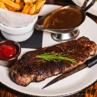 Grilled strip steak, garnished with rosemary, served with gravy, fries, and ketchup.