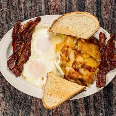 Breakfast plate with potatoes, bacon, fried eggs, and toast.