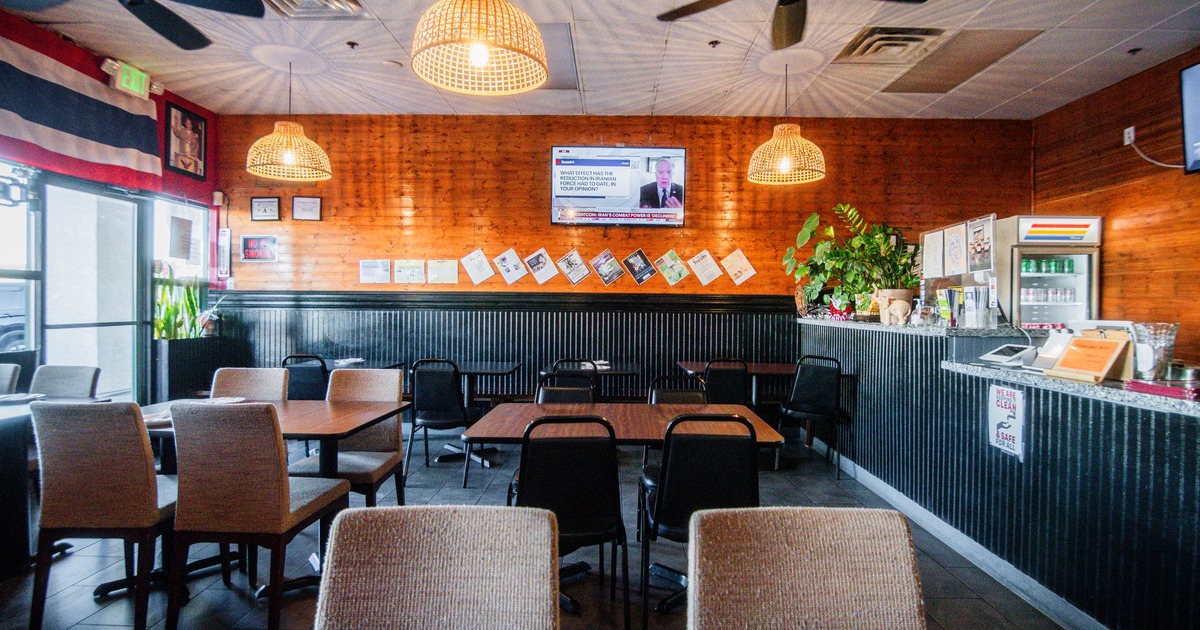 Interior of a restaurant with wooden walls, pendant lights, tables, chairs, and a TV