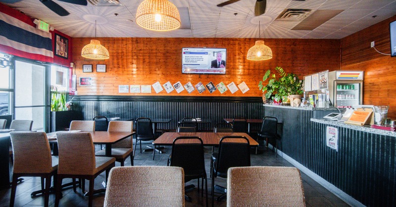 Interior of a restaurant with wooden walls, pendant lights, tables, chairs, and a TV