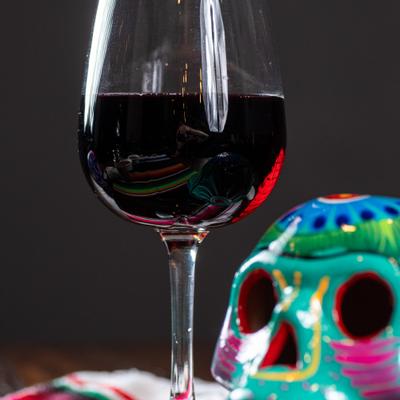 A glass of red wine beside a colorful decorative skull.