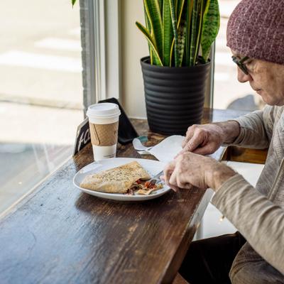 Person enjoying a sandwich and a beverage at a wooden table in a cafe.