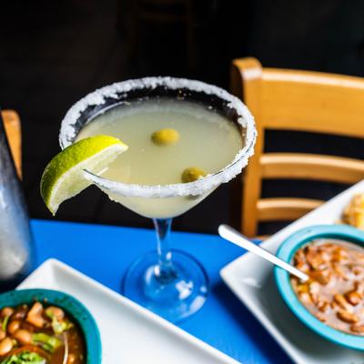 Mexican Martini cocktail served in a salt-rimmed glass, garnished with olives and a lime wedge.