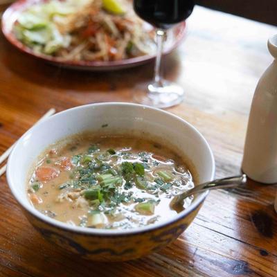 Thai soup on a table, red wine and another dish in the background.