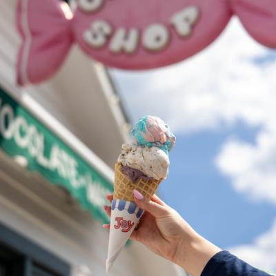 A hand holds a triple-scoop ice cream cone against a bright blue summer sky.