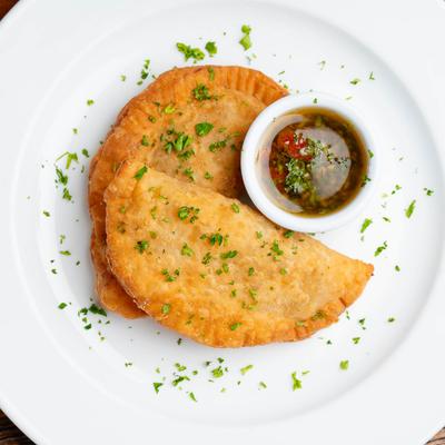 Two empanadas sprinkled with herbs, served with dipping sauce.
