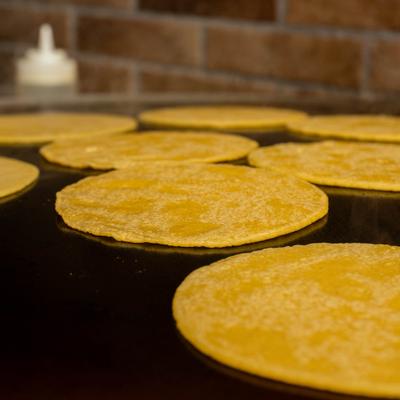 Corn tortillas are being toasted on a hot flat-top grill.