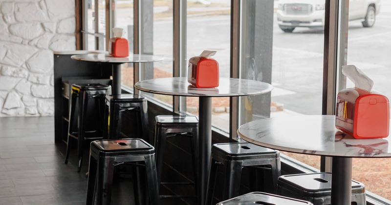 Modern interior, high-top tables and metal stools by windows, hanging plants