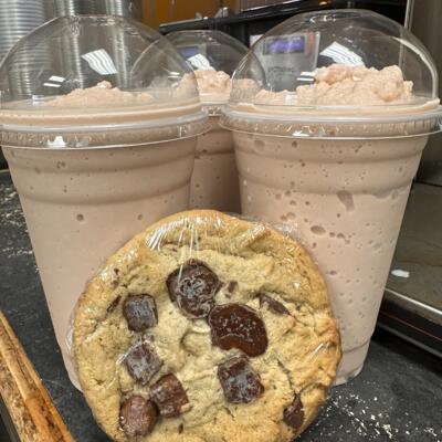 a chocolate chip cookie propped up against three frappuccinos, all sitting on a countertop.